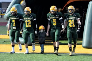 HONORARY TEAM MEMBER - Boyd football players (from left) Cole Meador, Michael Partin, Blake McDonald and Adrian Nelson walk onto the field with 5-year-old Gabrial Latham prior to their game against Godley Sept. 14. The team draws inspiration from the youngster, who is fighting neuroblastoma. Messenger photo by Kelly Guess
