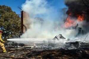 HOT JOB - A firefighter douses flames that destroyed a vacant house in  Sycamore Thursday. Messenger photo by Joe Duty