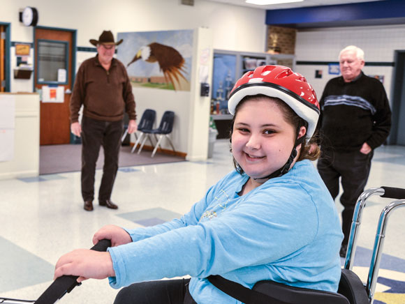 MOVING GIFT - After school last Friday, Charlie Young and Bill Silver (background left to right), members of AMBUCS Inc. service organization, presented McCarroll Middle School seventh grader Aneliz Medina an AmTryke, a modified tricycle that accommodates riders of all ages, sizes and physical limitations. The provides a fun form of therapy for the 14-year-old, who is recovering from a stroke. Messenger photo by Joe Duty
