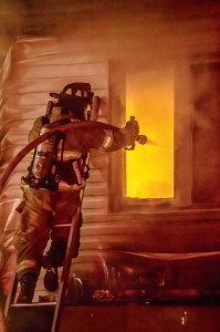 DIRECT ATTACK - An Alvord firefighter sprays water through a second-story window at a fire at a duplex near downtown Alvord Tuesday night. No one was injured in the blaze. Messenger photo by Joe Duty