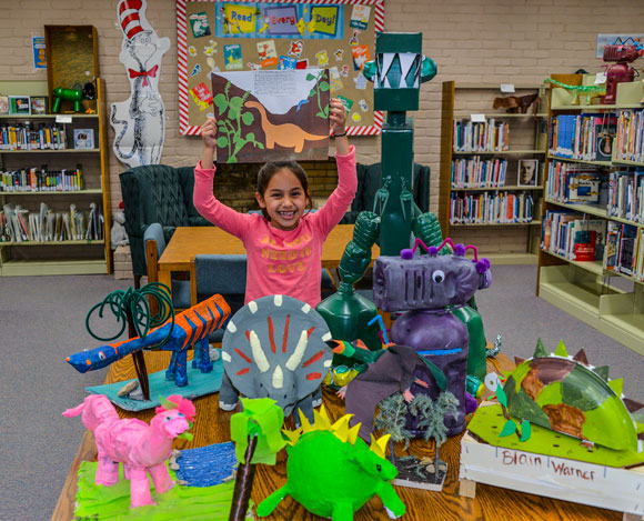 DINO DISPLAY - Bridgeport Elementary second grader Montserrat Uribe-Baeza shows a dinosaur she made from recycled products. The creations of 122 students are on display at the Bridgeport Public Library through next week, which is when the library will hold its used books sale. Messenger photo by Joe Duty