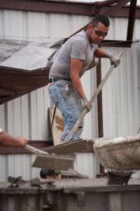 POURING AWAY - Production manager Joel Moraza smooths concrete slated to be the reinforced outer walls of a storm shelter. Felipe Bustos stands on the ground below using a machine to vibrate and settle the wet concrete into the form. Messenger photo by Jimmy Alford